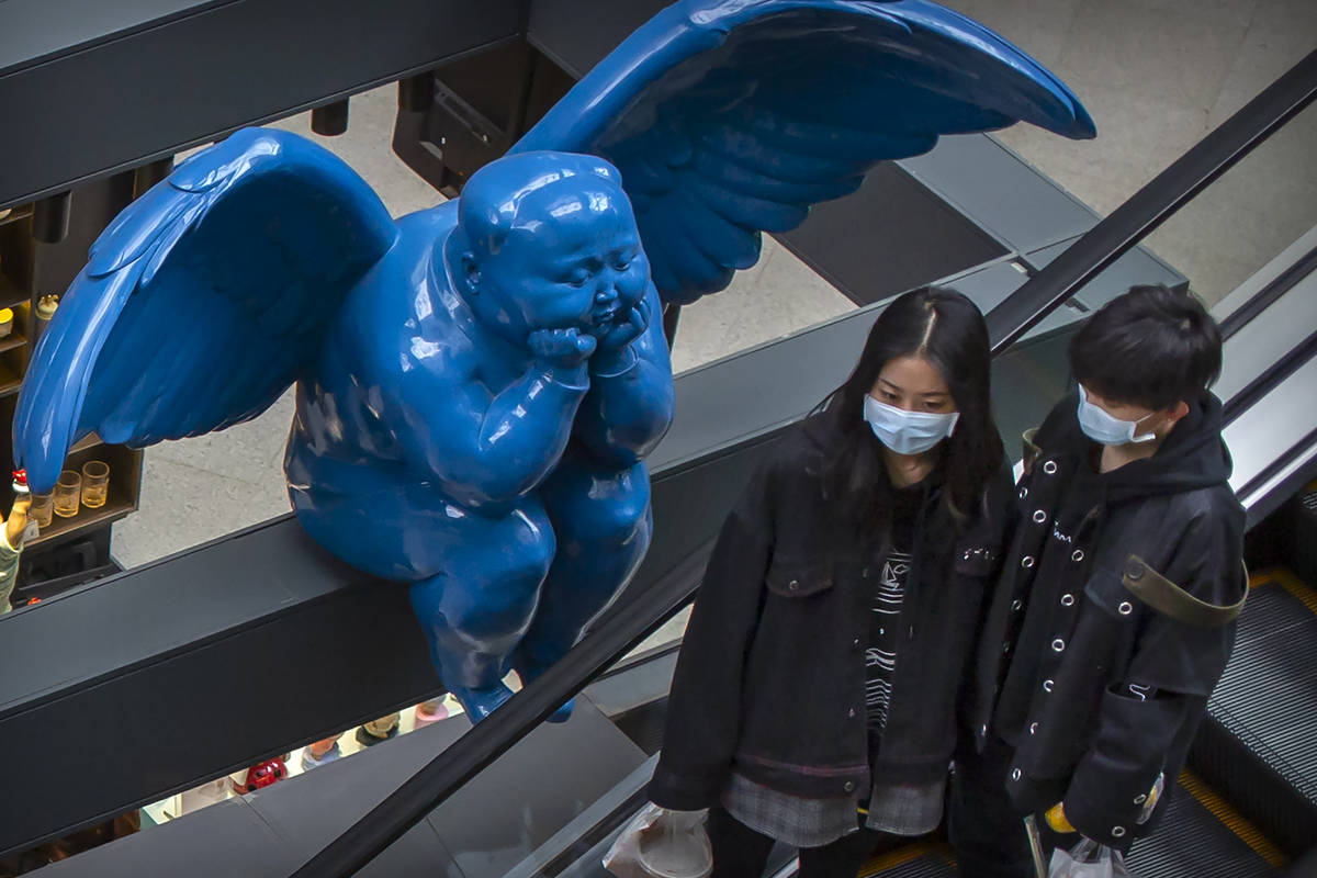People wearing face masks ride an escalator near a winged statue at an upscale shopping mall in ...