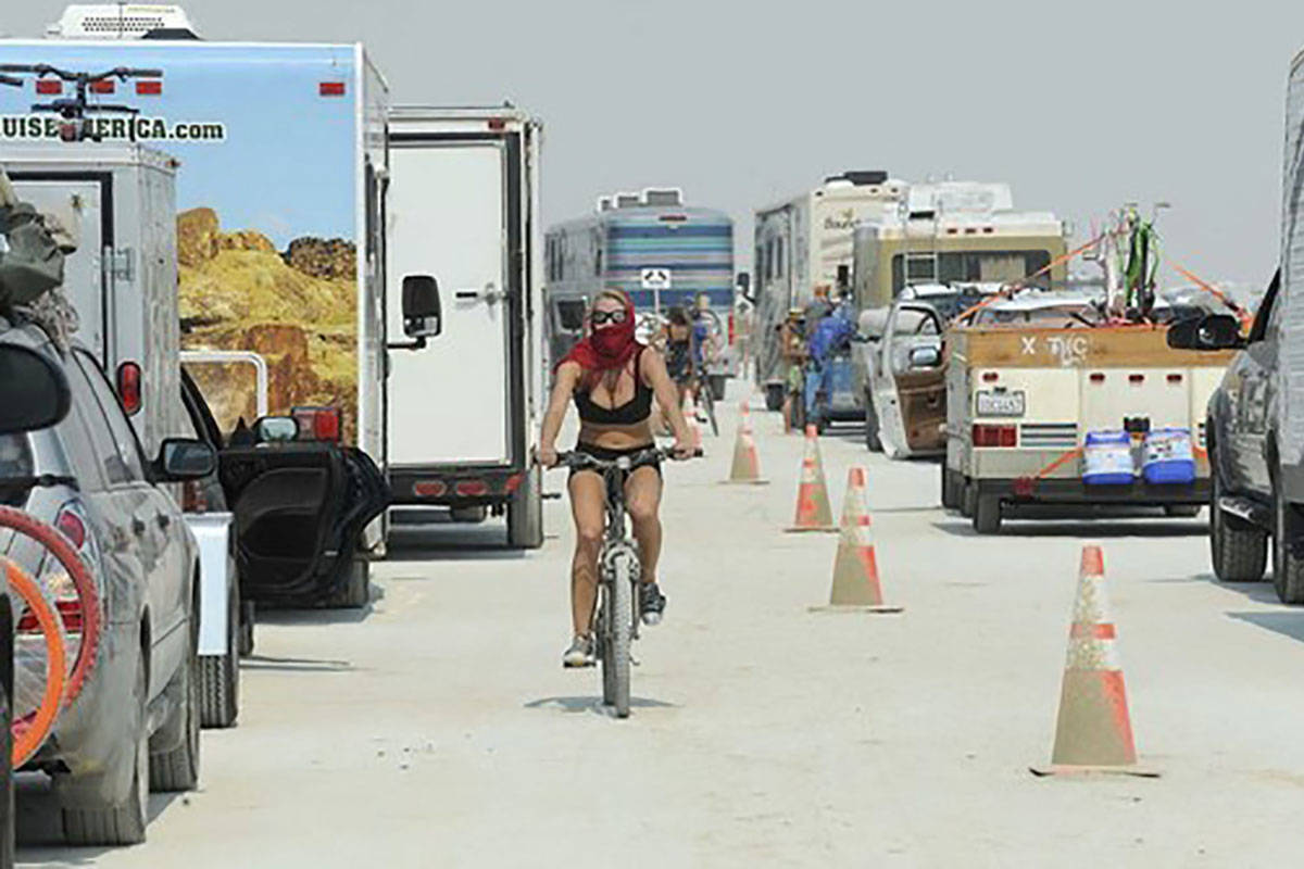 A woman rides her bike between cars waiting to enter Burning Man in Gerlach in 2013. The San Fr ...