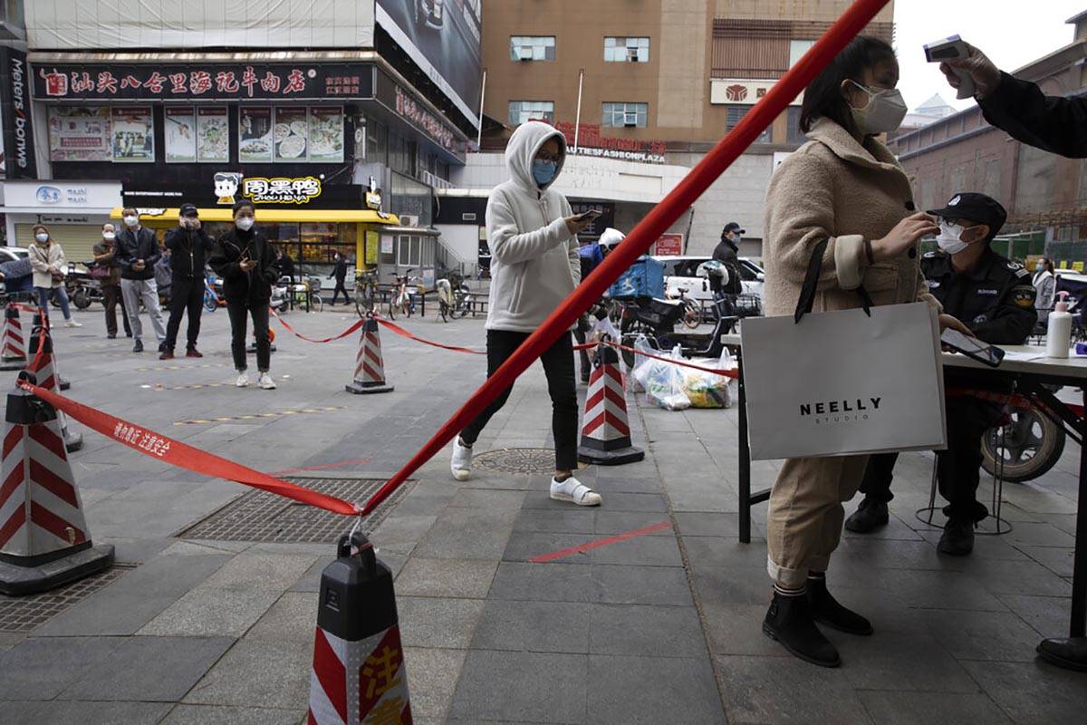 Residents wearing masks to protect against the spread of the coronavirus line up to enter a sup ...