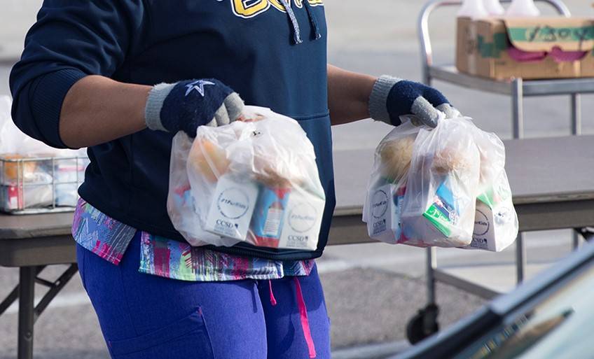 A worker hands out breakfast and lunch packages to families at a school in March 2020. (Rachel ...