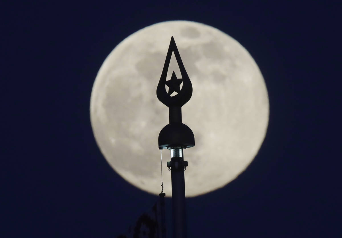 A nearly full moon rises behind a top of the flagpole on the State Flag Square in Minsk, Belaru ...