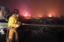 A firefighter hoses down burnt cars in the aftermath of a fire that destroyed more than 3,500 c ...