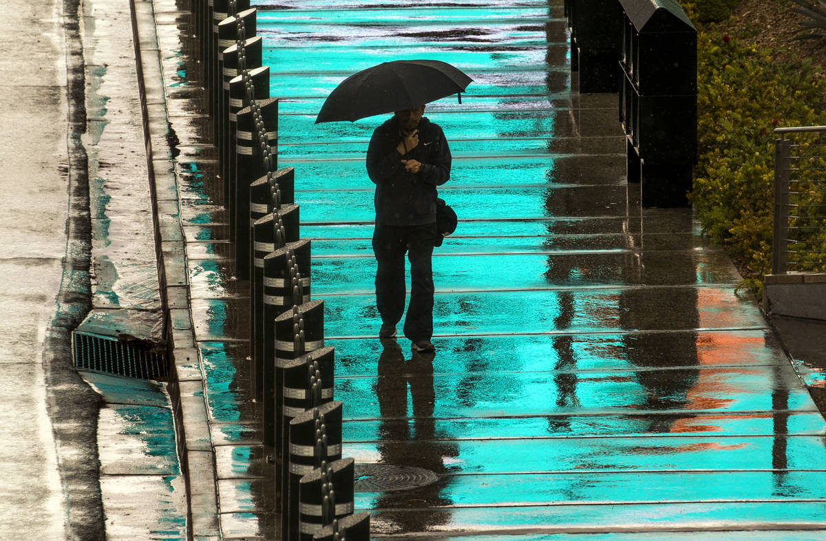 A pedestrian is bathed in blue light from a lighted sign above as he walks in the rain about th ...