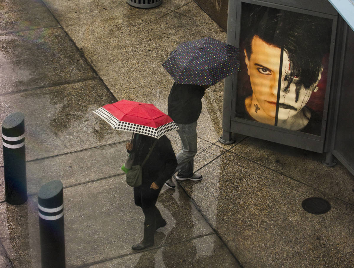 Pedestrians stand under umbrellas in the rain at a bus stop about the Fashion Show mall along t ...