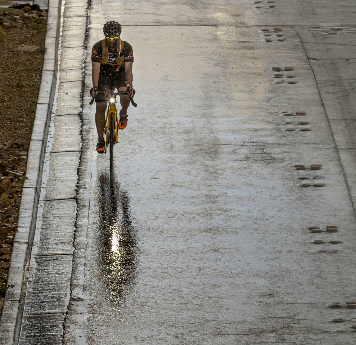 A cyclist wearing a face mask rides in the rain down the Las Vegas Strip past the Fashion Show ...