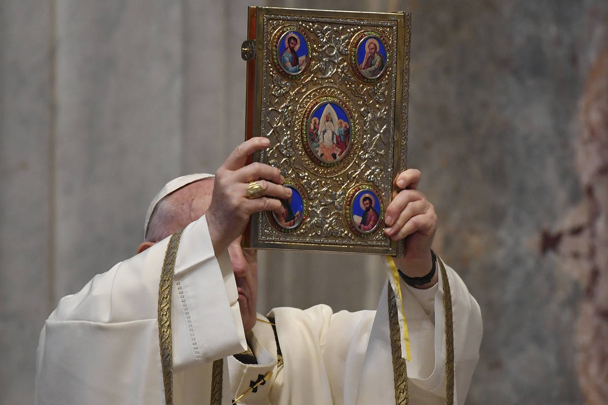 Pope Francis holds up the Holy Gospel book during Easter Sunday Mass, inside an empty St. Peter ...