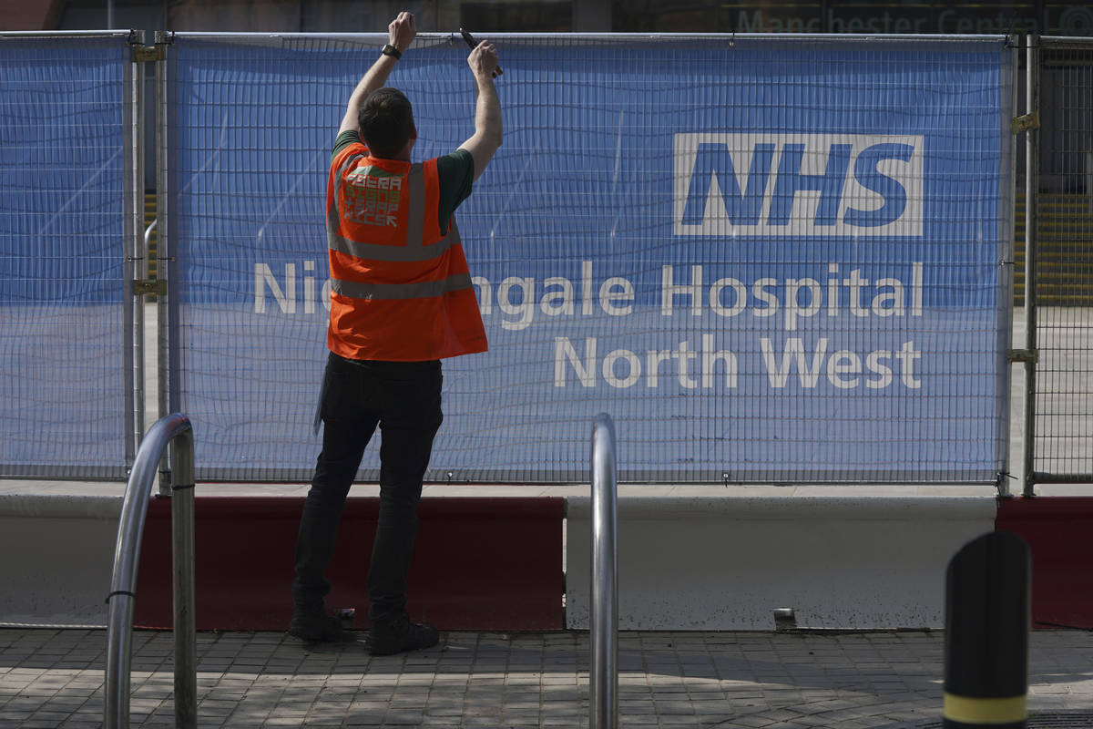 A worker puts signs on fencing outside the newly setup coronavirus Nightingale Hospital North W ...