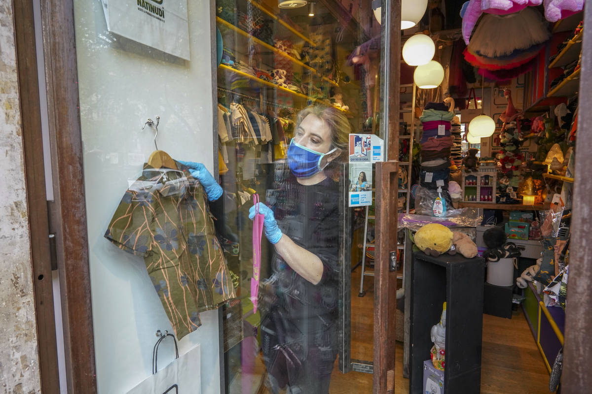 Camilla Cocchi wears a face mask and gloves as she adjusts her children's clothing shop window ...