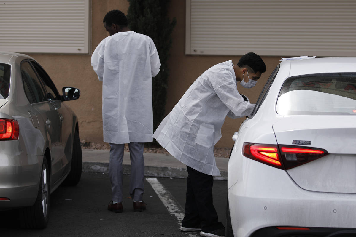 A caregiver, right, administers a coronavirus test to a person in a car at the Sahara West Urge ...