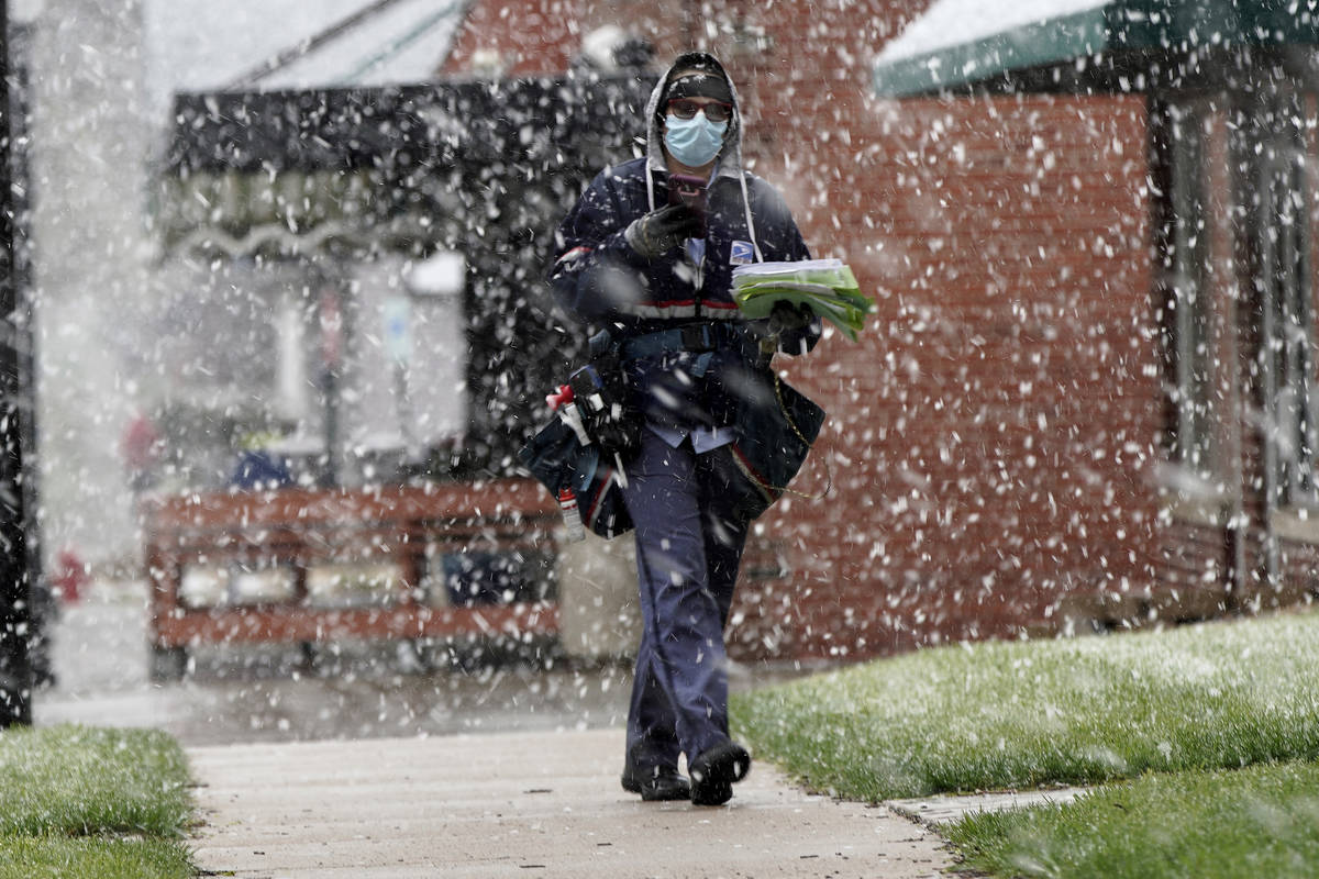 A mail carrier wears a face mask against COVID-19 as hedelivers mail in a spring snow storm in ...