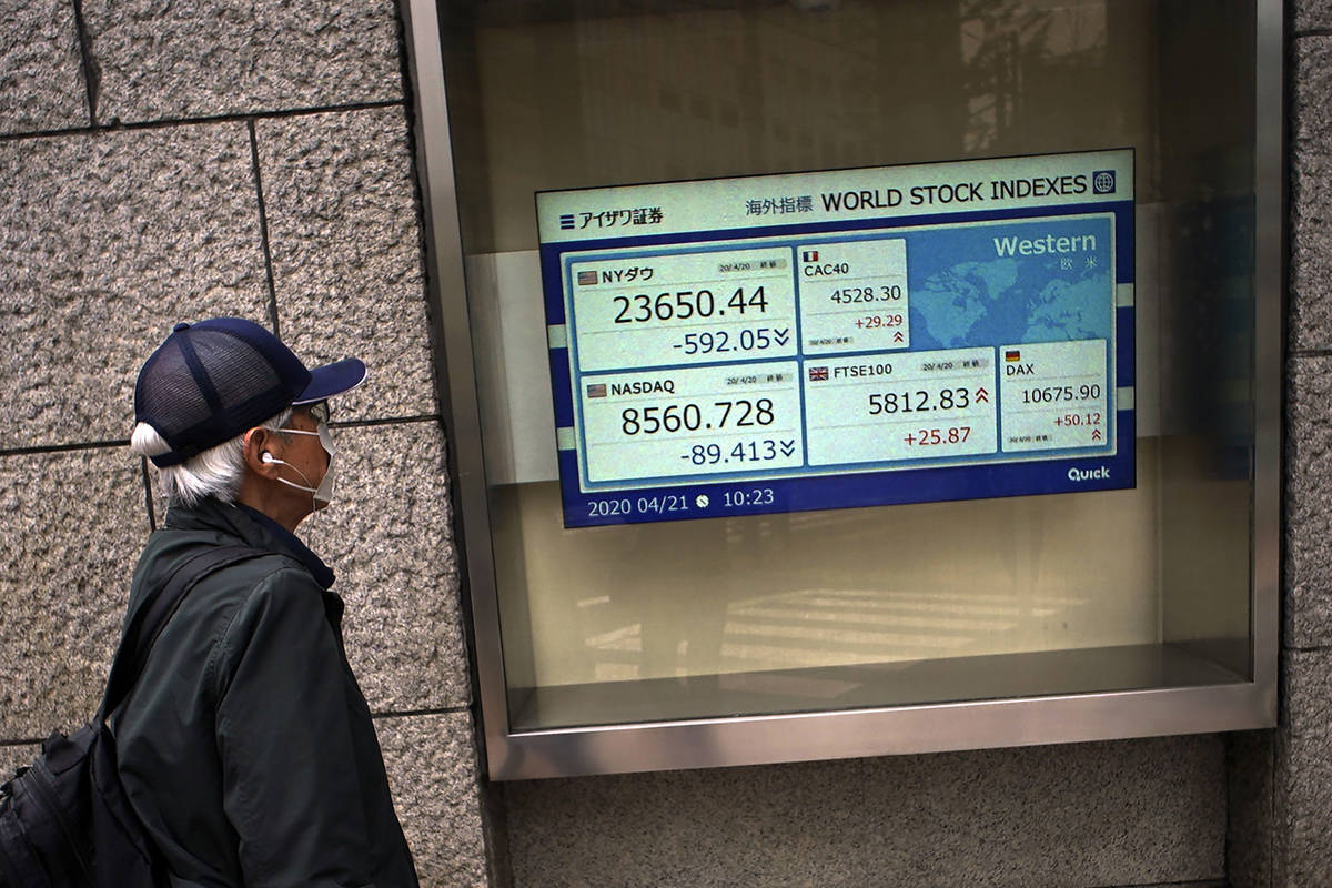 A man wearing a mask against the spread of the new coronavirus looks at an electronic stock boa ...