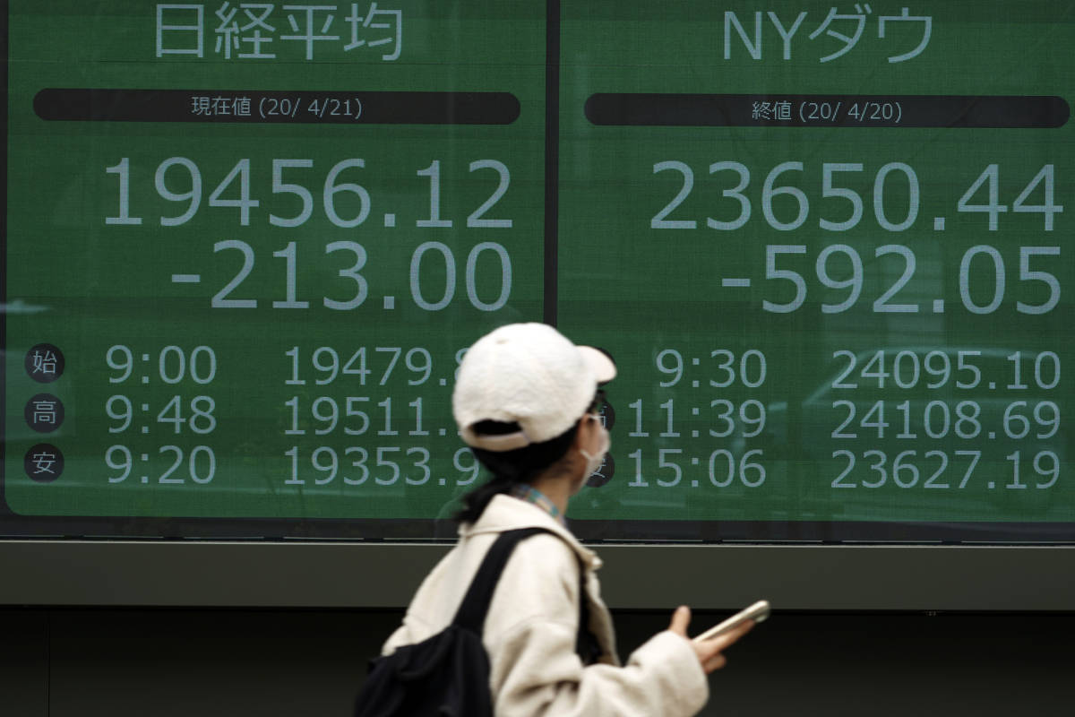 A woman wearing a mask against the spread of the new coronavirus walks past an electronic stock ...