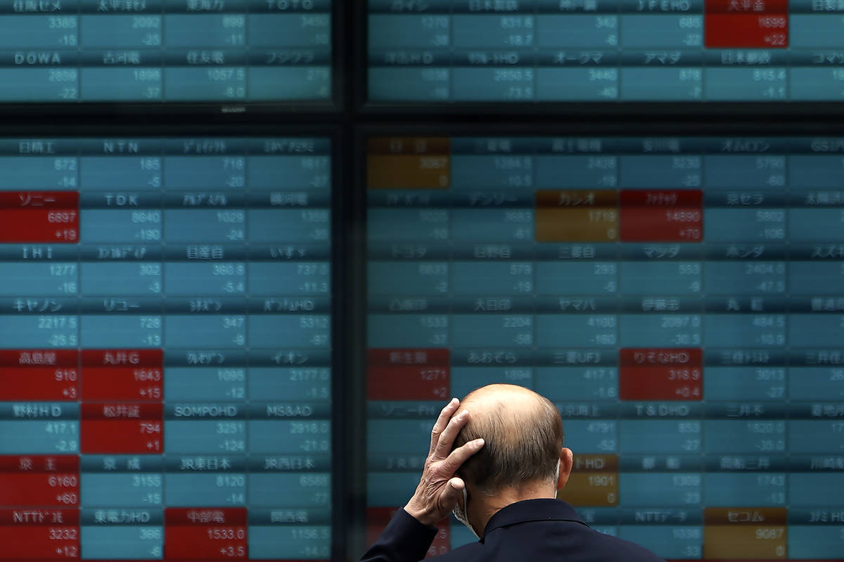 A man wearing a mask against the spread of the new coronavirus looks at an electronic stock boa ...