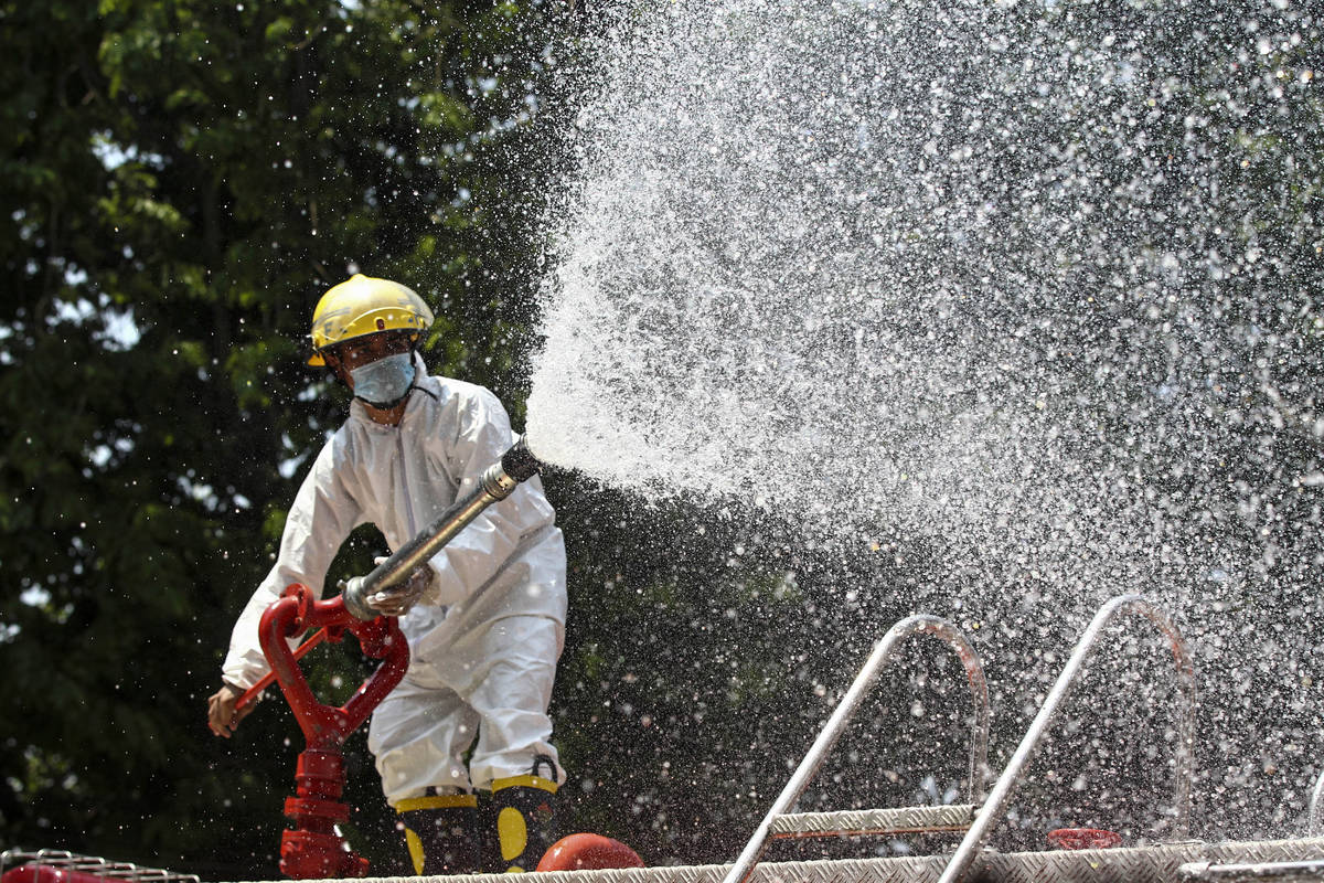 A member of the fire department wearing full protective gear sprays disinfectant from the fire ...