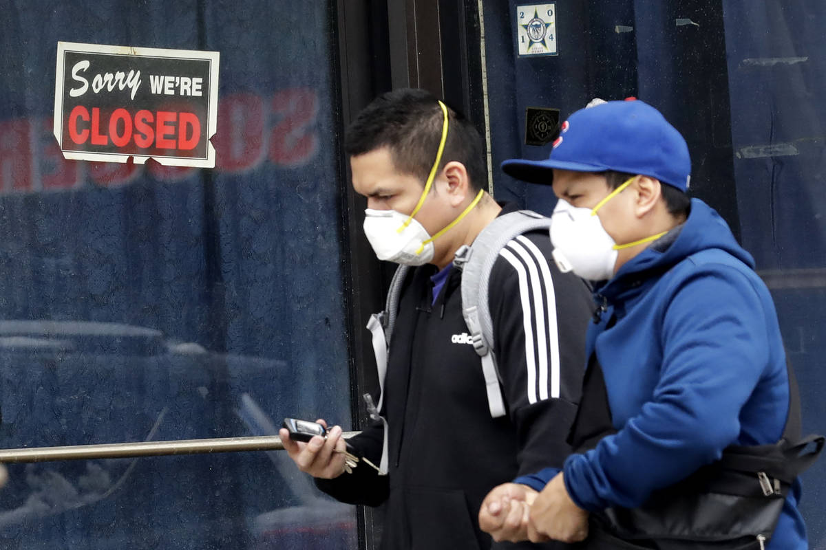 FILE - In this April 15, 2020 file photo, two people walk past a closed sign at a retail store ...