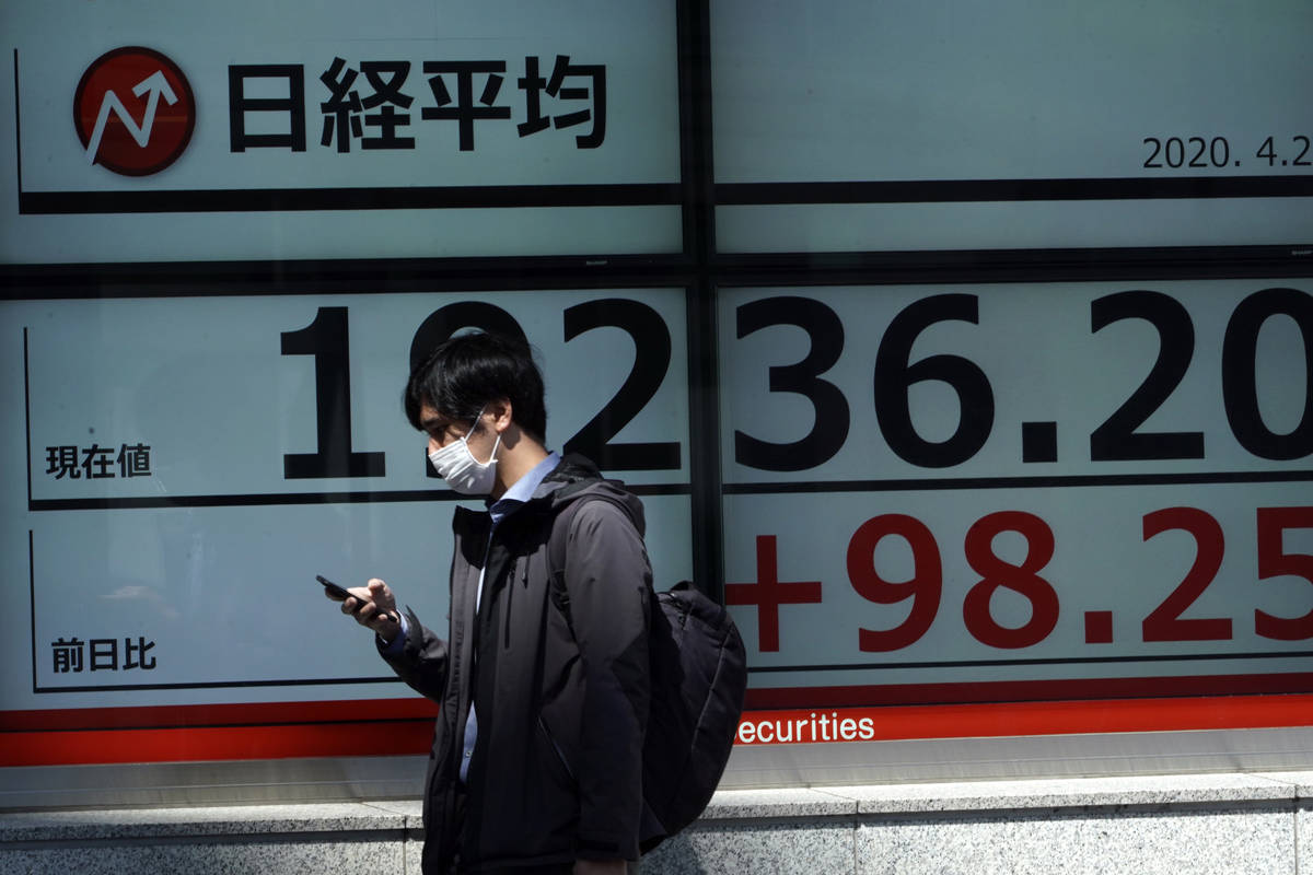 A man wearing a mask against the spread of the new coronavirus walks past an electronic stock b ...