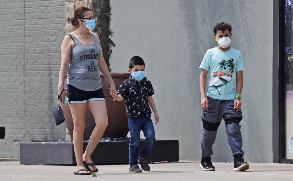 Amid concerns of the spread of COVID-19, a woman and two boys wear masks as they walk at a shop ...