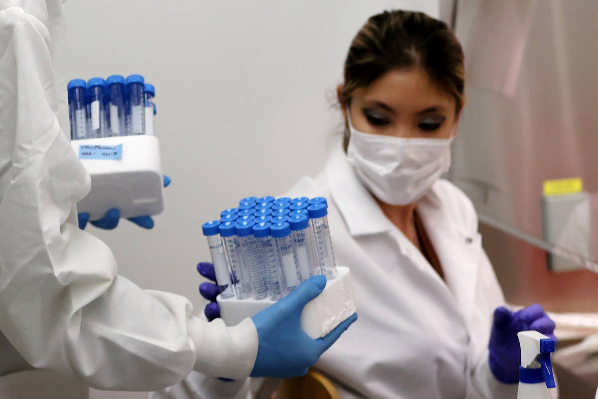 Lab manager Monika Karney, left, collects vials filled with viral transport medium from graduat ...