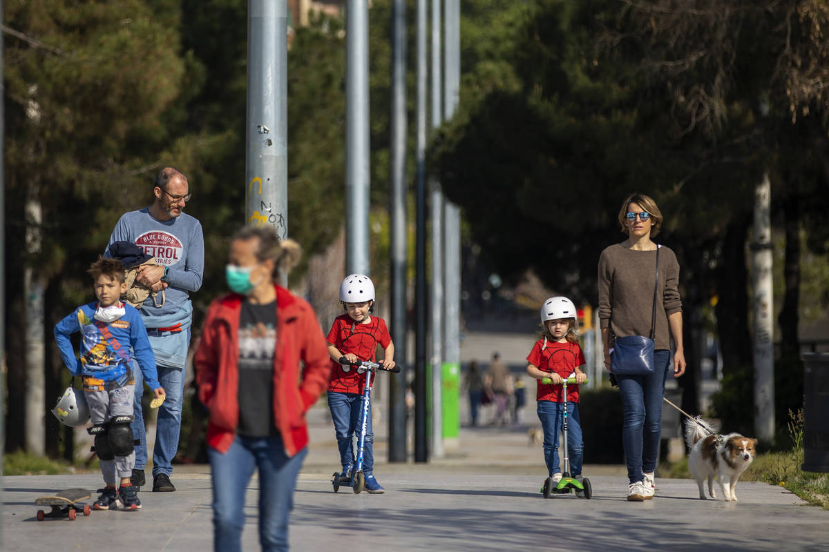 Families walk in the sunshine along a boulevard in Barcelona, Spain, Sunday, April 26, 2020, as ...