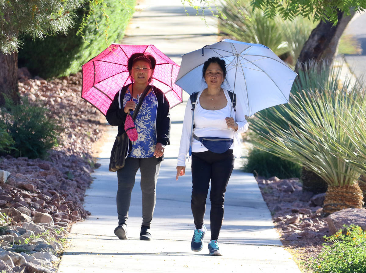 Elizabeth Pablo, left, and Florence Abrogena, both of Henderson, hold umbrellas to shield thems ...