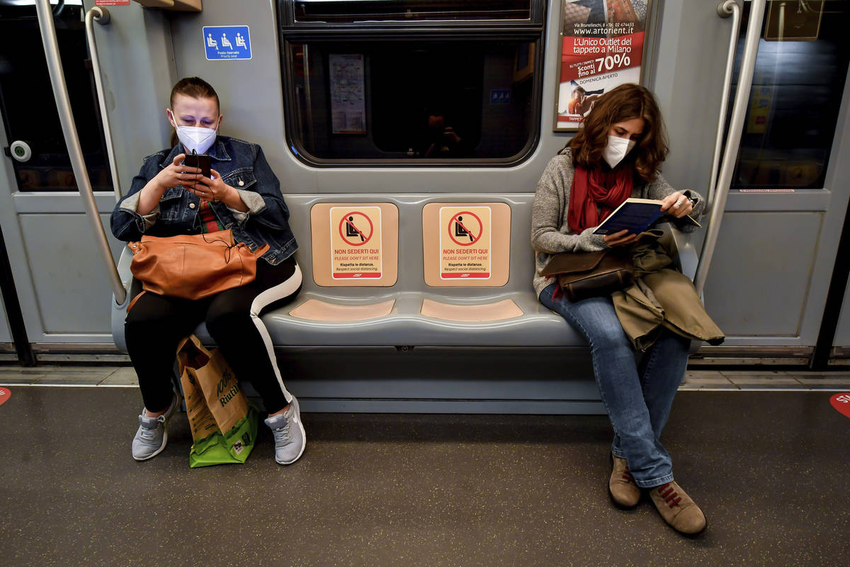 Women read a book and check their smartphones in a subway train as signs reading ' please do no ...