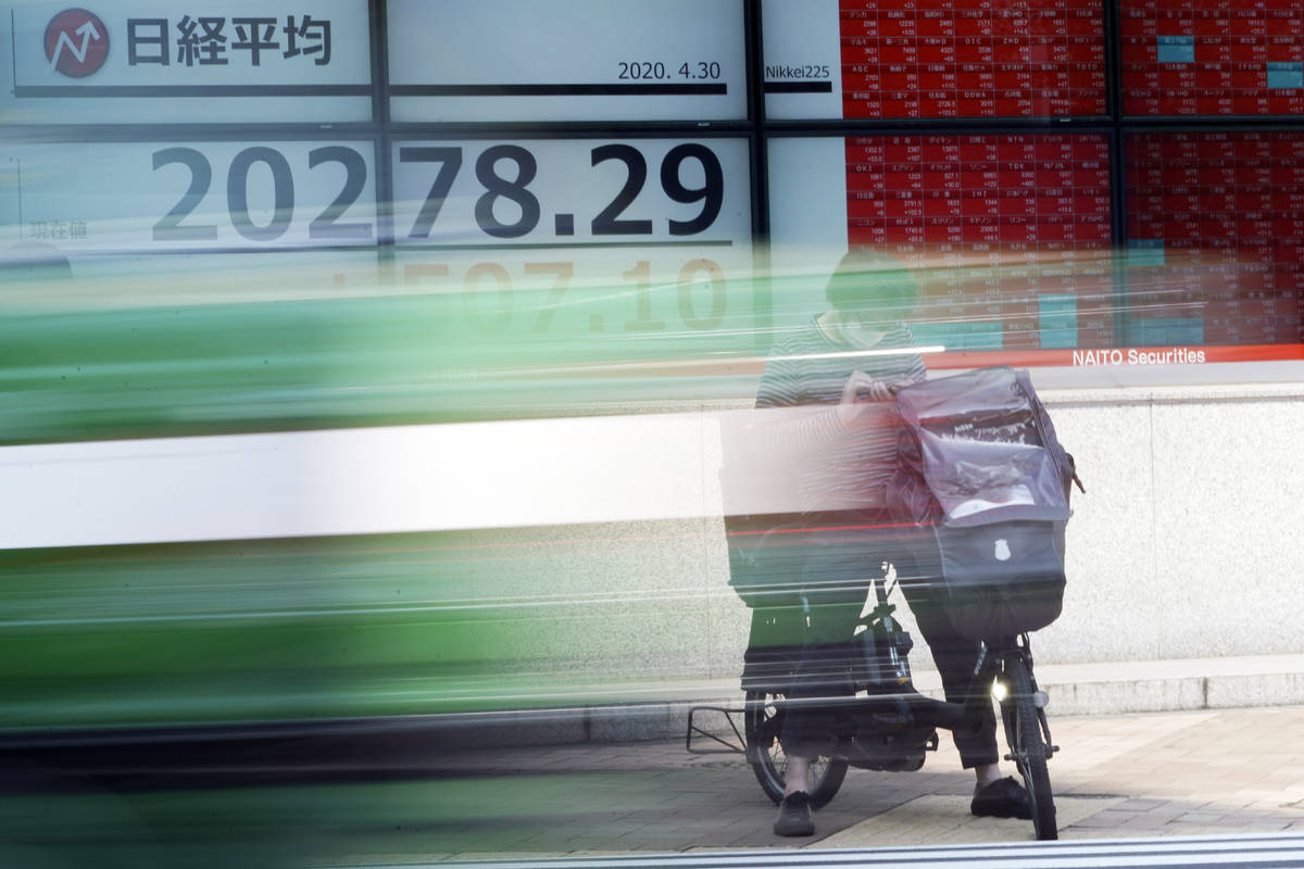 A man rides a bicycle in front of an electronic stock board showing Japan's Nikkei 225 index at ...