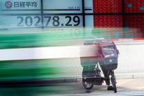 A man rides a bicycle in front of an electronic stock board showing Japan's Nikkei 225 index at ...