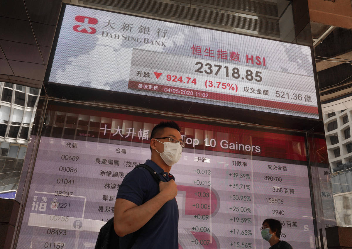 A man wearing face mask walks past a bank electronic board showing the Hong Kong share index at ...