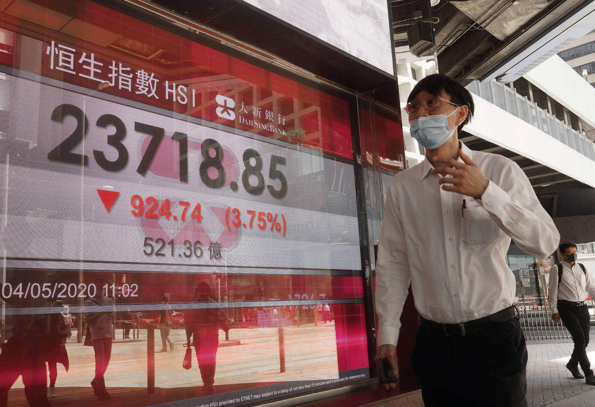 A man wearing face mask walks past a bank electronic board showing the Hong Kong share index at ...