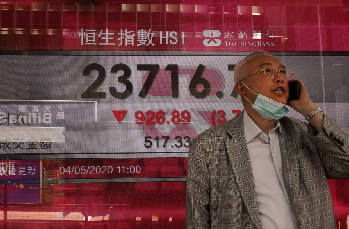 A man wearing face mask walks past a bank electronic board showing the Hong Kong share index at ...