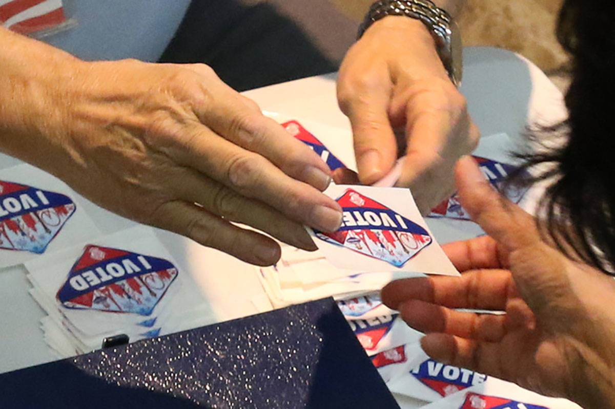 A worker hands out "I Voted " sticker to a voter at a polling station at Galleria Mall on Tuesd ...