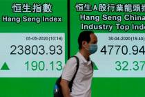 A man wearing face mask walks past a bank electronic board showing the Hong Kong share index Tu ...