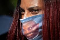A woman wears a face covering with the likeness of shooting victim Ahmaud Arbery printed on it ...