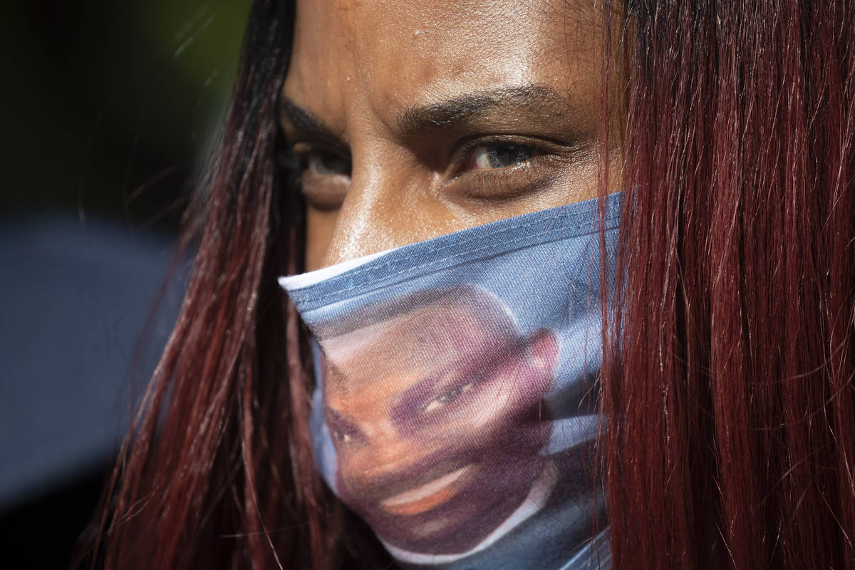 A woman wears a face covering with the likeness of shooting victim Ahmaud Arbery printed on it ...