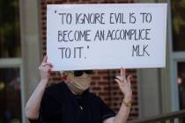 A person holds a sign while watching a rally to protest the shooting of Ahmaud Arbery, Friday, ...