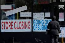 A woman looks at signs at a store closed due to COVID-19 in Niles, Ill., Wednesday, May 13, 202 ...
