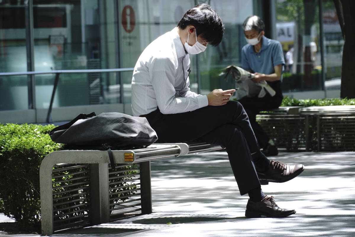 Men wearing face mask to help curb the spread of the coronavirus take a rest in Tokyo Thursday, ...