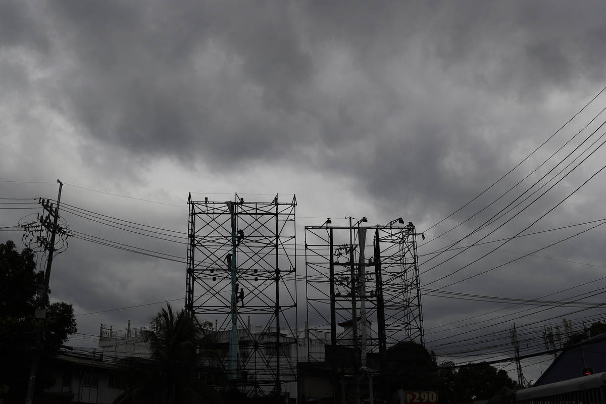 Dark clouds envelop the skies as workers fold a billboard to prepare for the coming of typhoon ...
