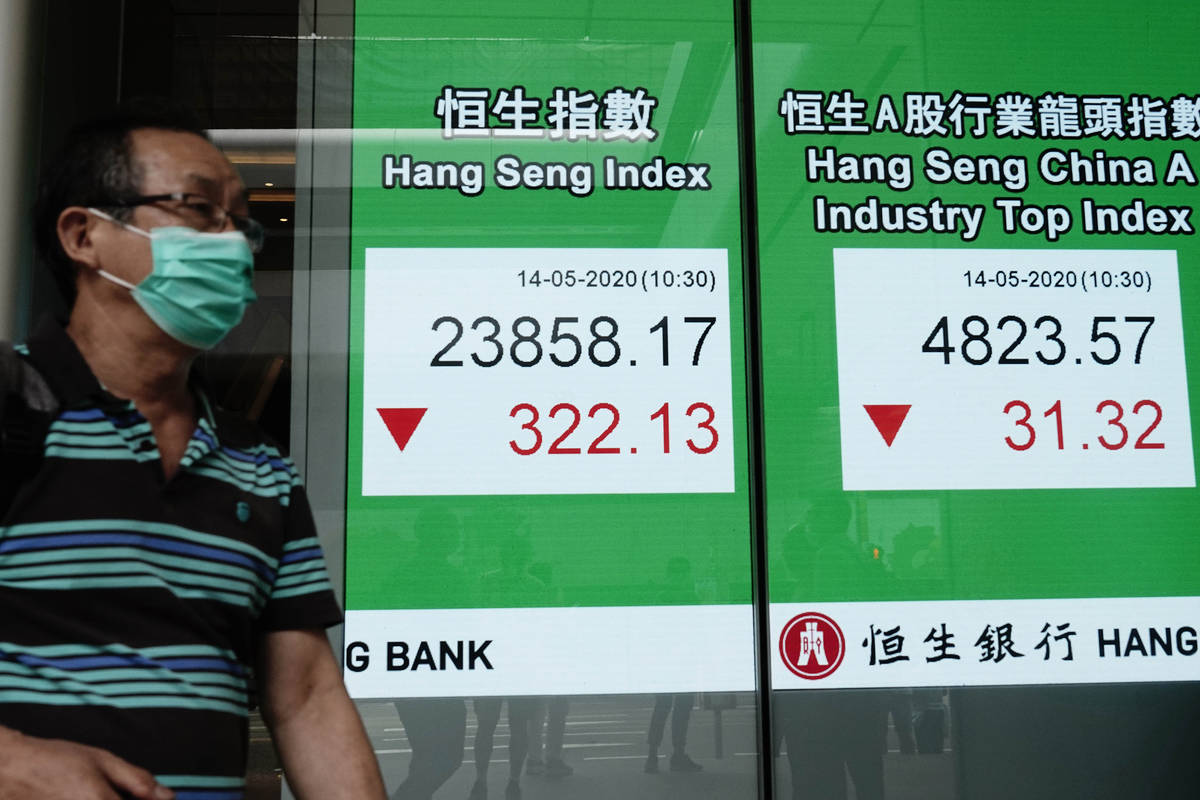 A man wearing face mask walks past a bank electronic board showing the Hong Kong share index at ...