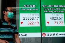 A man wearing face mask walks past a bank electronic board showing the Hong Kong share index at ...