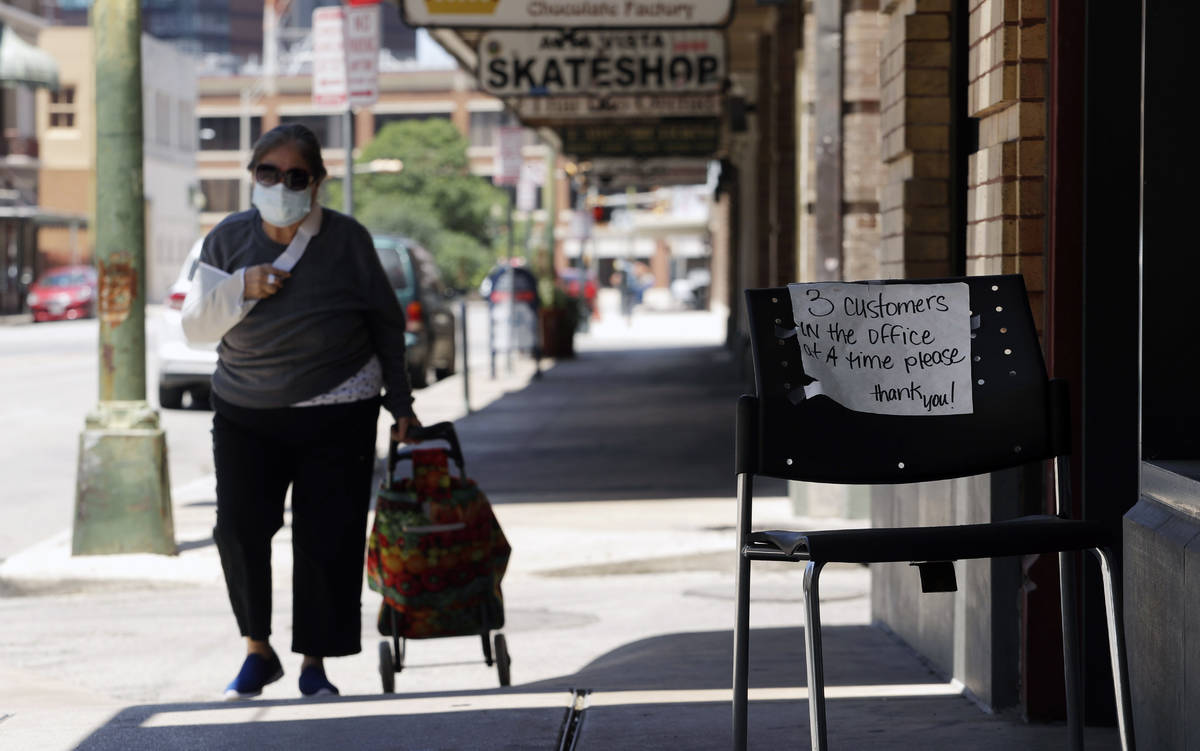 A woman wearing a face mask for protection against COVID-19 passes a business that has reopened ...