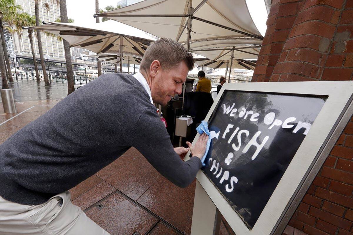 Alec Owes wipes a sign alerting customers that the Sydney Cove Oyster Bar is open as stage 1 of ...