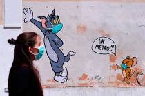A woman wearing a face mask passes by a mural featuring William Hanna and Joseph Barbera' s cha ...