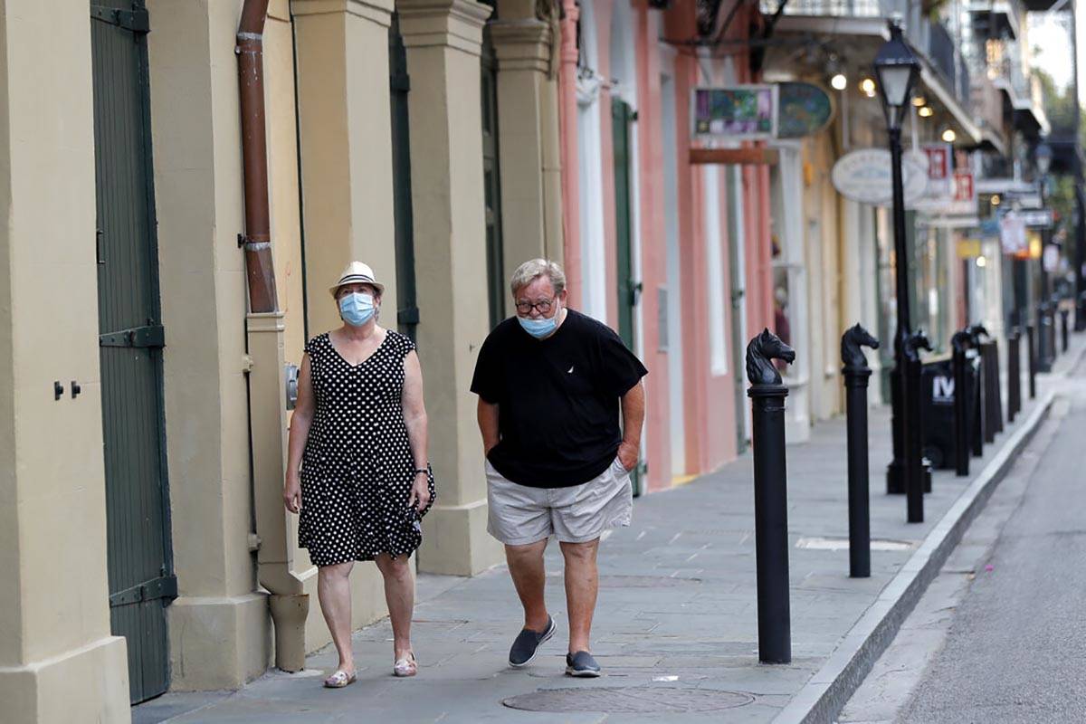 A couple walks past shuttered businesses impacted by the coronavirus epidemic, on Royal St, in ...
