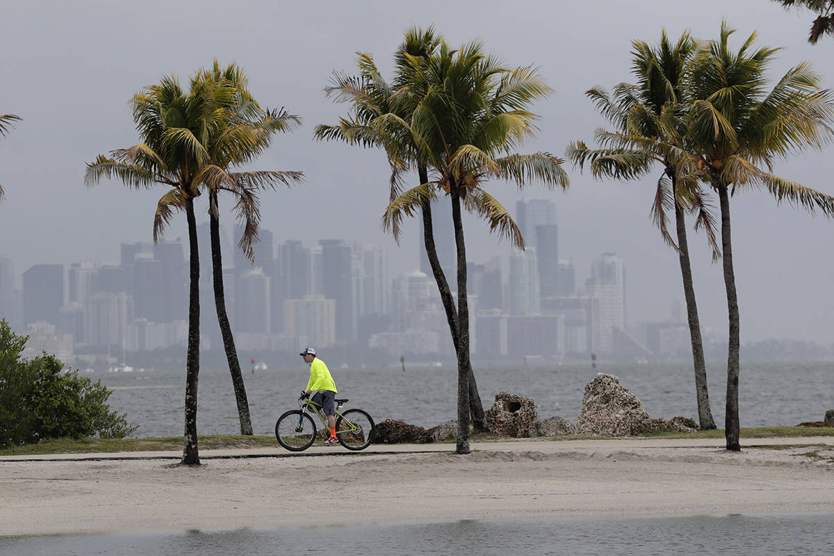 The Miami skyline is shrouded in clouds as a cyclist rides along Biscayne Bay at Matheson Hammo ...