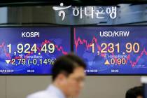 A currency trader walks near the screens showing the Korea Composite Stock Price Index (KOSPI), ...