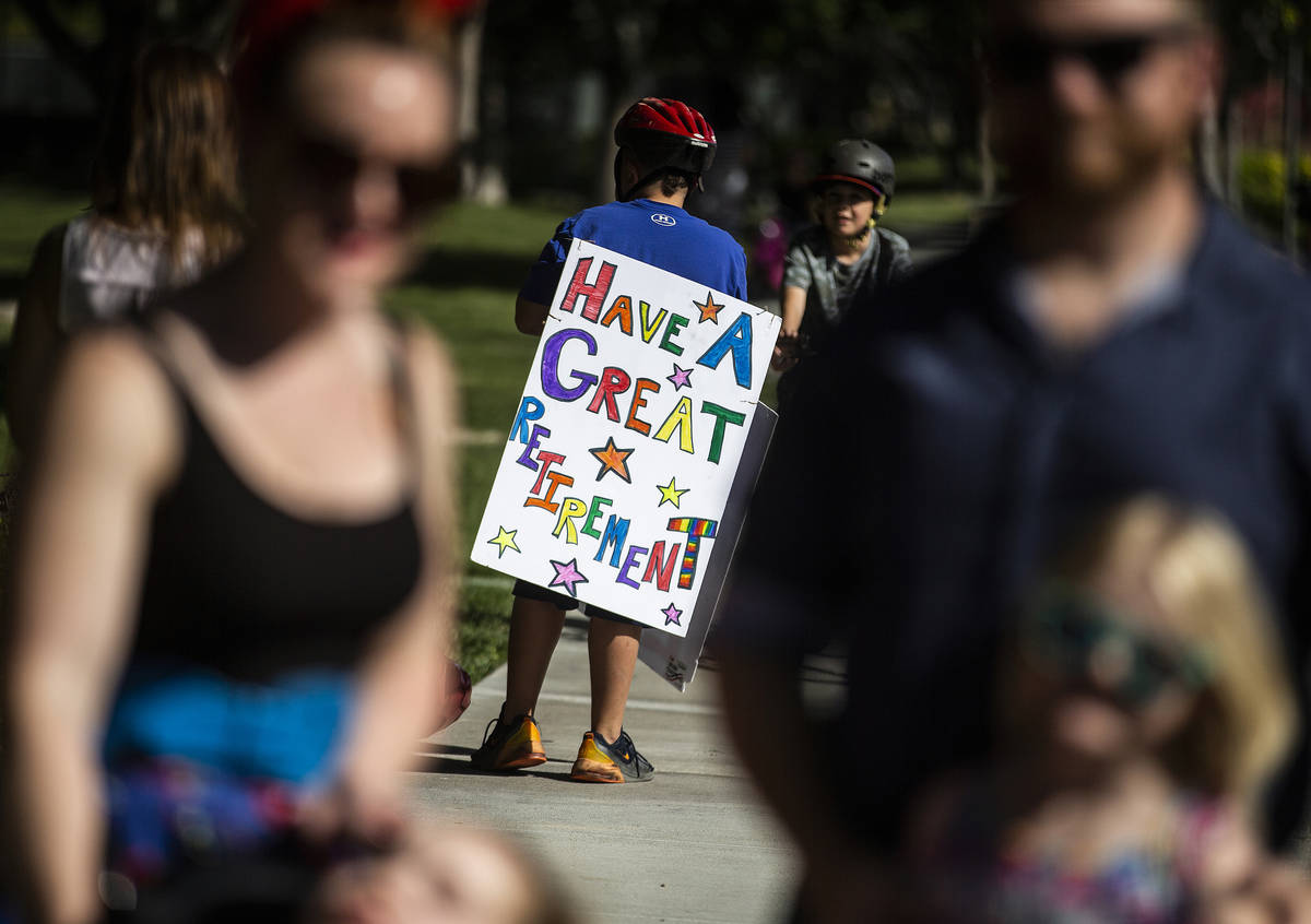 Children hold signs sending well wishes during a “drive-by” retirement party for ...