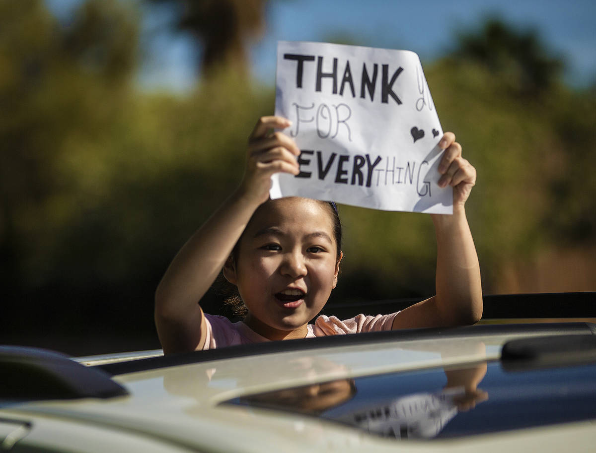 Children hold signs sending well wishes in a line of cars during a “drive-by” ret ...