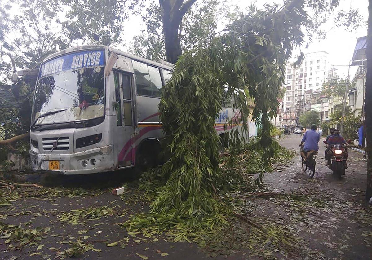 Commuters move past a tree branch precariously hanging after cyclone Amphan hit the region, in ...