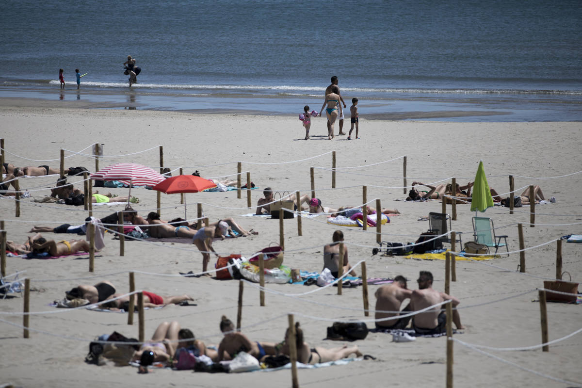 Sunbathers lie in an area marked by cordons of ropes and wooden stakes to enforce social distan ...